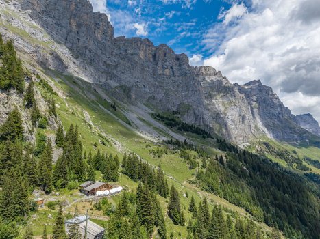 Aerial view of the Tallihutte SAC mountain hut nestled among steep rocky cliffs lush green meadows and dense coniferous forests in Innertkirchen Bern Switzerland.