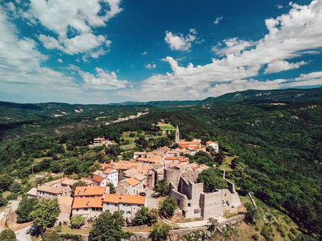 Aerial view of Boljun Castle and the historic hilltop village with stone houses and red tiled roofs surrounded by lush green forests in Boljun Istria County Croatia.