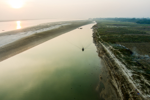 Aerial view of a small boat navigating the calm waters of the Padma River at sunset with sandy banks and rural landscape in Rajshahi Rajshahi Division Bangladesh.