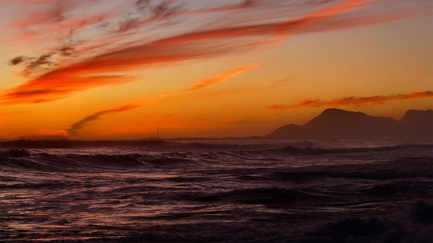 Aerial view of crashing ocean waves under a vibrant sunset sky with orange clouds and mountain silhouettes Cape Town Western Cape South Africa. Aerial view of crashing ocean waves under a vibrant sunset sky with orange clouds and mountain silhouettes Cape Town Western Cape South Africa.
