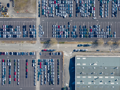Aerial view of a vast geometrically arranged car park showcases rows of vehicles in contrasting white blue and red hues punctuated by the stark lines of architecture Sausheim Grand Est France.