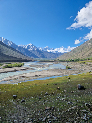 View of the Penzi La road winding through the Zanskar valley with a river flowing between snow capped mountains under a clear blue sky in Zanskar Ladakh India.