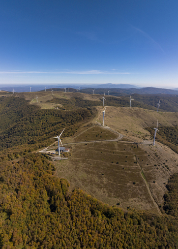 Aerial view of wind turbines situated on rolling hills covered with autumn forests under a clear blue sky in Bulgaria. Aerial view of wind turbines situated on rolling hills covered with autumn forests under a clear blue sky in Bulgaria.