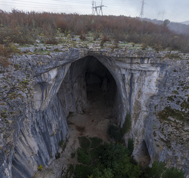 Aerial view of Prohodna Cave a natural rock bridge with large karst openings surrounded by autumn foliage and rocky terrain in Karlukovo Lovech Bulgaria. Aerial view of Prohodna Cave a natural rock bridge with large karst openings surrounded by autumn foliage and rocky terrain in Karlukovo Lovech Bulgaria.
