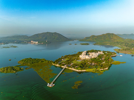 Aerial view of Taj Lake Palace situated on an island in Lake Pichola surrounded by lush green hills clear water and a bridge connecting to the shore Udaipur Rajasthan India. Aerial view of Taj Lake Palace situated on an island in Lake Pichola surrounded by lush green hills clear water and a bridge connecting to the shore Udaipur Rajasthan India.