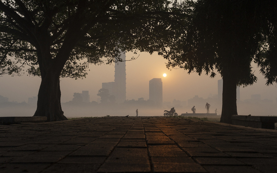 View of the sun rising through the mist silhouetting buildings and trees casting a golden glow on the stone path Kolkata West Bengal India. View of the sun rising through the mist silhouetting buildings and trees casting a golden glow on the stone path Kolkata West Bengal India.