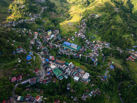 Aerial view of the town center nestled among lush green hills and rice terraces under bright sunlight in Banaue Cordillera Administrative Region Philippines.