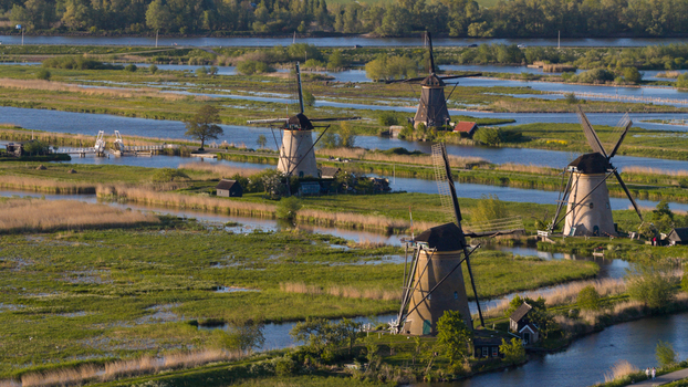 Aerial view of Kinderdijk windmills along water canals surrounded by green fields and reeds under warm sunlight Kinderdijk South Holland Netherlands. Aerial view of Kinderdijk windmills along water canals surrounded by green fields and reeds under warm sunlight Kinderdijk South Holland Netherlands.