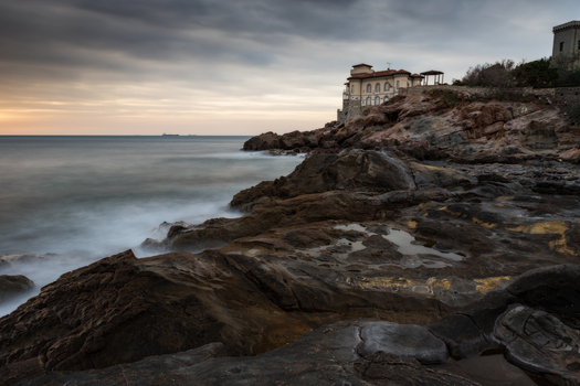 View of Castello del Boccale on the rocky cliffs of Calafuria with waves crashing against the shore under a dramatic cloudy sky Calafuria Toscana Italy.