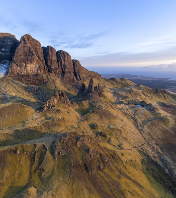 Aerial view of The Storr rock formations and the Old Man of Storr pinnacle on rugged grassy slopes under a clear blue sky Isle of Skye Scotland United Kingdom. Aerial view of The Storr rock formations and the Old Man of Storr pinnacle on rugged grassy slopes under a clear blue sky Isle of Skye Scotland United Kingdom.