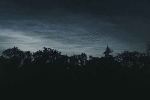 View of noctilucent clouds glowing in the night sky above a dark treeline on Vormsi Laane County Estonia.