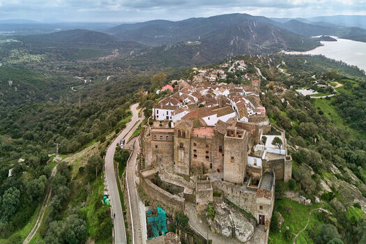 Aerial view of the old weathered stone castle atop a hill contrasting with the surrounding lush green landscape and distant lake Castellar de la Frontera Andalucía Spain. Aerial view of the old weathered stone castle atop a hill contrasting with the surrounding lush green landscape and distant lake Castellar de la Frontera Andalucía Spain.