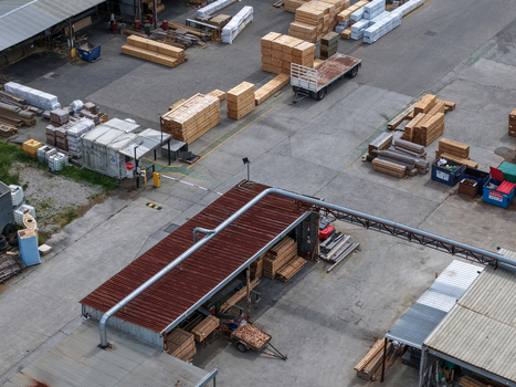 Melbourne Australia 25 September 2026 Aerial view of a timber factory yard featuring stacks of processed wood industrial machinery and transport trailers on a concrete lot.