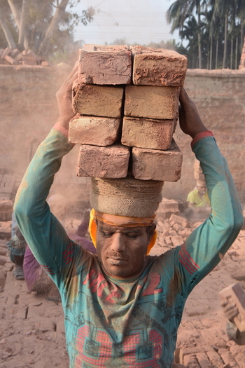 Kushtia District Khulna Division Bangladesh 28 November 2020 View of a worker carrying a heavy stack of bricks on his head at a dusty brickyard. Kushtia District Khulna Division Bangladesh 28 November 2020 View of a worker carrying a heavy stack of bricks on his head at a dusty brickyard.