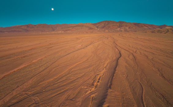 Aerial view of the arid Atacama Desert landscape with intricate dry river channels and distant mountains under a clear blue sky with a visible moon in San Pedro de Atacama Antofagasta Chile. Aerial view of the arid Atacama Desert landscape with intricate dry river channels and distant mountains under a clear blue sky with a visible moon in San Pedro de Atacama Antofagasta Chile.