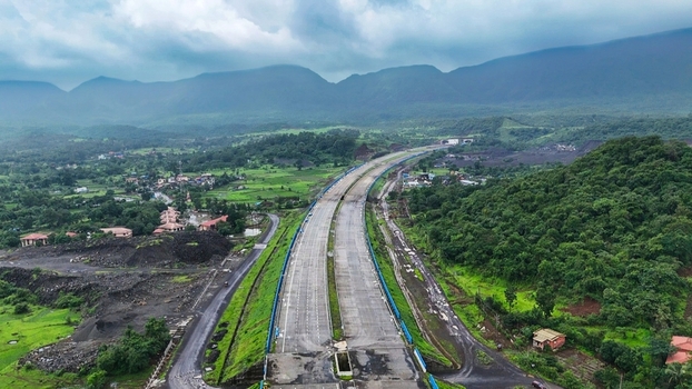 Aerial view of Delhi Mumbai Expressway winding through lush green hills and rural landscape under a cloudy sky in Badlapur Maharashtra India. Aerial view of Delhi Mumbai Expressway winding through lush green hills and rural landscape under a cloudy sky in Badlapur Maharashtra India.