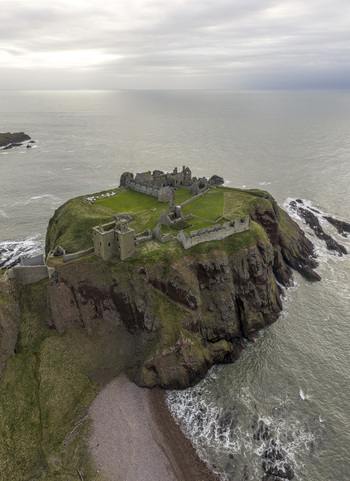 Aerial view of Dunnottar Castle ruins on a dramatic cliff edge overlooking the North Sea under an overcast sky Stonehaven Scotland United Kingdom. Aerial view of Dunnottar Castle ruins on a dramatic cliff edge overlooking the North Sea under an overcast sky Stonehaven Scotland United Kingdom.