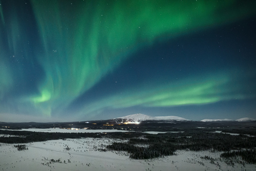Aerial view of the Aurora Borealis illuminating the night sky over the snow covered landscape and frozen lake of Yllasjarvi Lapland Finland.