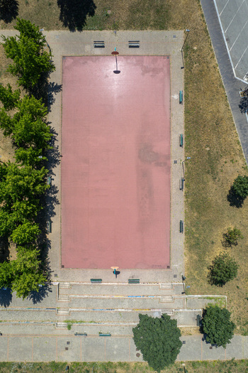 Aerial view of a pink outdoor basketball court surrounded by lush green trees and park benches in Turin Piedmont Italy. Aerial view of a pink outdoor basketball court surrounded by lush green trees and park benches in Turin Piedmont Italy.