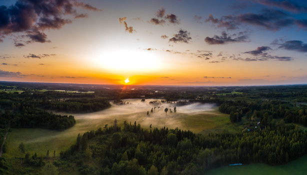 Aerial view of a misty field surrounded by dense forest during a vibrant sunset in Latvia. Aerial view of a misty field surrounded by dense forest during a vibrant sunset in Latvia.