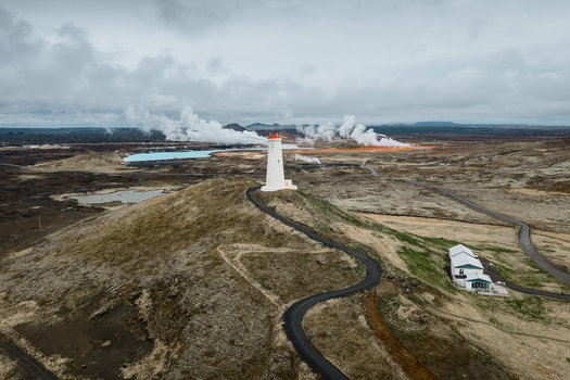 Aerial view of the Reykjanesviti lighthouse standing on a hill with geothermal steam rising in the background and a winding road leading to the structure in Reykjavik Reykjavikurborg Iceland. Aerial view of the Reykjanesviti lighthouse standing on a hill with geothermal steam rising in the background and a winding road leading to the structure in Reykjavik Reykjavikurborg Iceland.