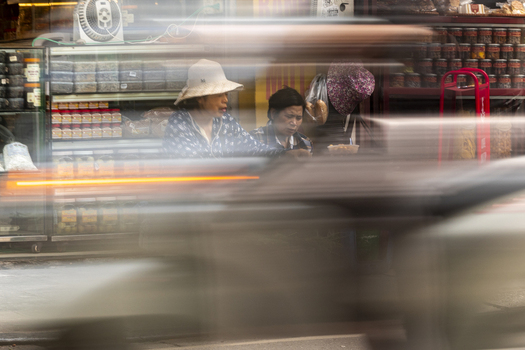 Hanoi Ha Noi Vietnam 11 November 2025 View of two women sitting in front of a shop with motion blur from passing traffic creating a dynamic urban atmosphere.
