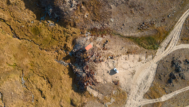 Aerial view of Deosai National Park featuring a small building with a red roof and a white vehicle parked on a dirt track in the rugged landscape of Skardu Gilgit Pakistan.