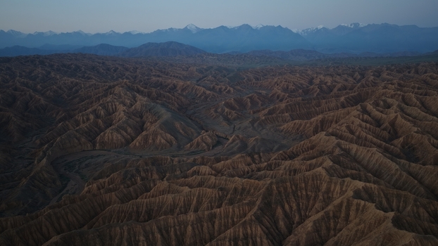 Aerial view of the rugged badlands and canyons of Issyk Kul with snow capped mountains in the distance in Issyk Kul Region Kyrgyzstan. Aerial view of the rugged badlands and canyons of Issyk Kul with snow capped mountains in the distance in Issyk Kul Region Kyrgyzstan.