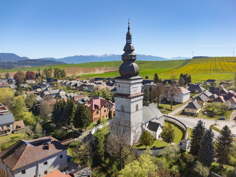 Aerial view of the historic St. Matthew s Church tower and traditional houses surrounded by green fields and distant mountains under a clear blue sky in Partizanska Lupca Zilina Region Slovakia. Aerial view of the historic St. Matthew s Church tower and traditional houses surrounded by green fields and distant mountains under a clear blue sky in Partizanska Lupca Zilina Region Slovakia.