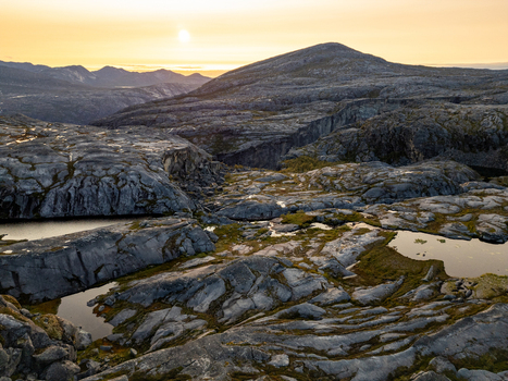 Aerial view of Hellmojuvet canyon featuring rugged rocky terrain small pools of water and distant mountains under the warm glow of the sunset in Hamaroy Nordland Norway.