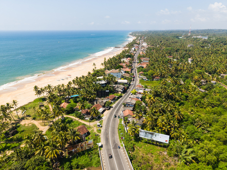 Aerial view of the coastal road winding along the sandy beach and turquoise ocean surrounded by lush palm trees in Galle Southern Province Sri Lanka.