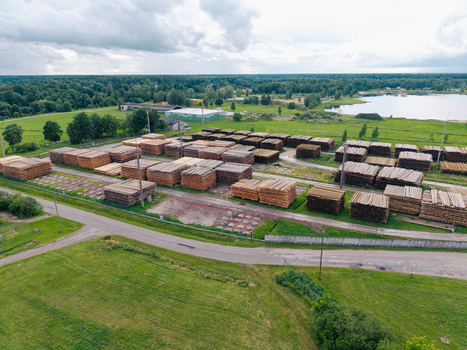 Aerial view of stacks of timber stored in a lumber yard surrounded by green fields forest and a lake in Brankas Jelgava Municipality Latvia. Aerial view of stacks of timber stored in a lumber yard surrounded by green fields forest and a lake in Brankas Jelgava Municipality Latvia.