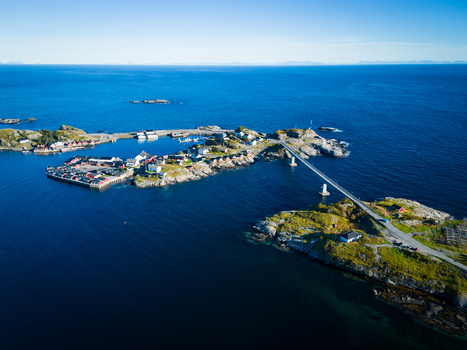 Aerial view of Hamnoy a fishing village with traditional red cabins on rocky islands connected by a bridge surrounded by the blue Norwegian Sea in Hamnoy Nordland Norway. Aerial view of Hamnoy a fishing village with traditional red cabins on rocky islands connected by a bridge surrounded by the blue Norwegian Sea in Hamnoy Nordland Norway.