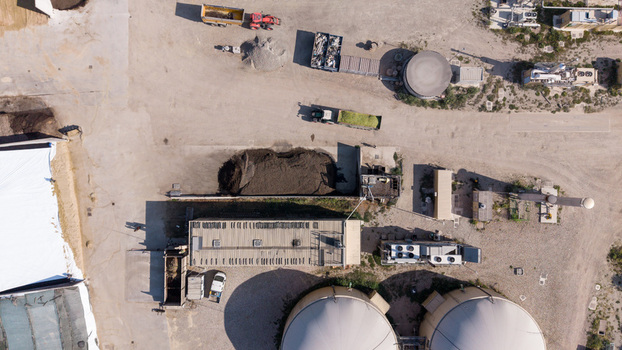 Aerial view of an agro farm biogas plant featuring large circular digesters piles of organic biomass and agricultural machinery on a gravel site in Milan Lombardy Italy. Aerial view of an agro farm biogas plant featuring large circular digesters piles of organic biomass and agricultural machinery on a gravel site in Milan Lombardy Italy.