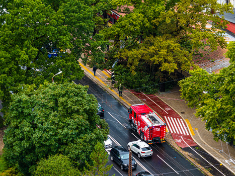 Riga Latvia 23 August 2026 Aerial view of a red fire truck parked on a city street with emergency responders lush green trees and passing cars in Riga.