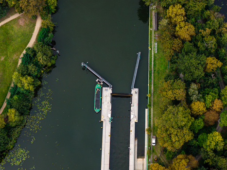 Aerial view of the Schleuse Spandau canal lock on the Havel river with a green cargo barge waiting in the water surrounded by lush trees and parkland in Berlin Berlin Germany.