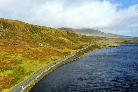 Aerial view of the rugged landscape near The Storr with a winding road along a loch surrounded by green hills under a cloudy sky in Portree Scotland United Kingdom.