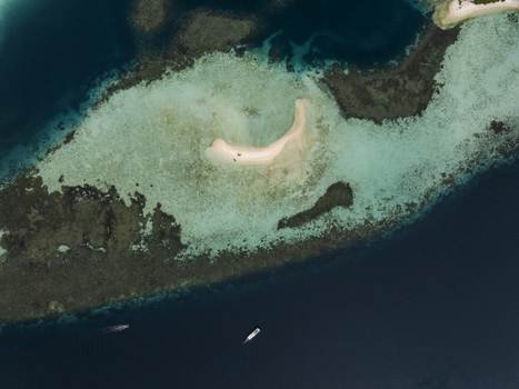 Aerial view of a small sandbar surrounded by vibrant coral reefs and turquoise waters near Flores East Nusa Tenggara Indonesia.