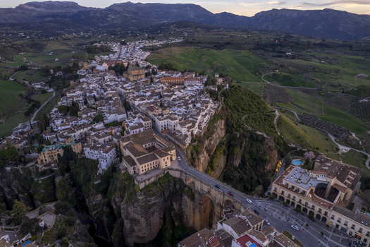 Aerial view of the historic town of Ronda perched on a deep gorge with the iconic Puente Nuevo bridge white buildings and surrounding green hills in Ronda Andalusia Spain. Aerial view of the historic town of Ronda perched on a deep gorge with the iconic Puente Nuevo bridge white buildings and surrounding green hills in Ronda Andalusia Spain.