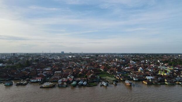 Aerial view of the Jakabaring riverside settlement with wooden houses boats moored along the Musi River and dense urban rooftops in Kecamatan Seberang Ulu I Sumatera Selatan Indonesia. Aerial view of the Jakabaring riverside settlement with wooden houses boats moored along the Musi River and dense urban rooftops in Kecamatan Seberang Ulu I Sumatera Selatan Indonesia.