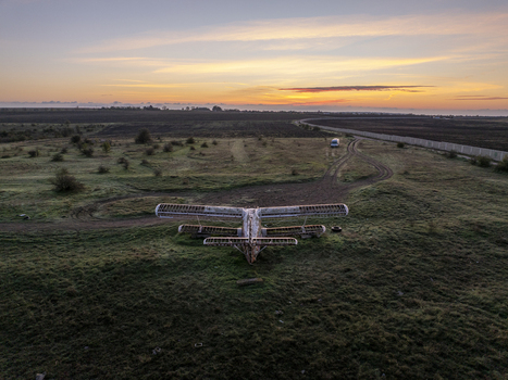 Aerial view of an abandoned skeletal biplane resting in a grassy field at sunset with a distant van in the landscape Bulgaria. Aerial view of an abandoned skeletal biplane resting in a grassy field at sunset with a distant van in the landscape Bulgaria.