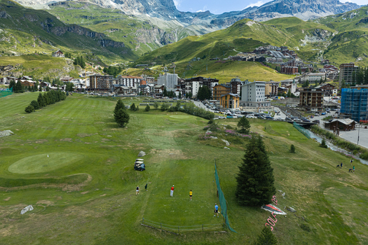 Aerial view of Breuil Cervinia golf course with players on the green surrounded by alpine mountains lush green slopes and resort buildings in Breuil Cervinia Aosta Valley Italy. Aerial view of Breuil Cervinia golf course with players on the green surrounded by alpine mountains lush green slopes and resort buildings in Breuil Cervinia Aosta Valley Italy.