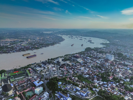 Aerial view of the Mahakam River flowing through Samarinda featuring the Islamic Center Mosque dense urban rooftops and cargo barges on the water in Samarinda Kalimantan Timur Indonesia. Aerial view of the Mahakam River flowing through Samarinda featuring the Islamic Center Mosque dense urban rooftops and cargo barges on the water in Samarinda Kalimantan Timur Indonesia.