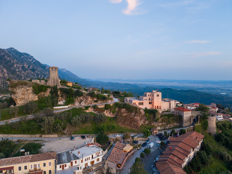 Aerial view of the historic Kruje Castle and stone clock tower on a rocky cliff with traditional red tiled rooftops and mountain peaks in Kruje Durres County Albania.