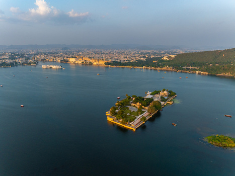 Aerial view of the historic Jag Mandir palace situated on an island in Lake Pichola surrounded by lush gardens and the cityscape of Udaipur Rajasthan India.
