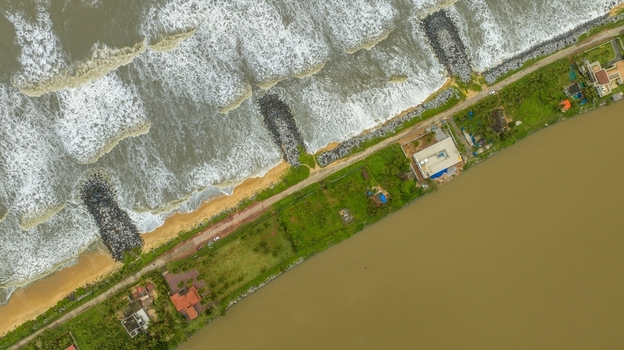 Aerial view of Mattu Beach showing the narrow land strip between the Arabian Sea and backwaters with stone breakwaters green vegetation and coastal houses in Udupi Karnataka India.