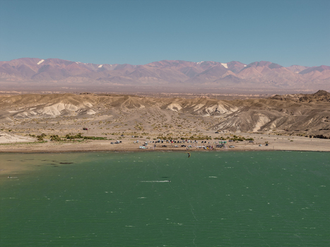 Aerial view of Cuesta del Viento reservoir with kiteboarders on the turquoise water surrounded by arid mountains and desert landscape in Rodeo San Juan Argentina.