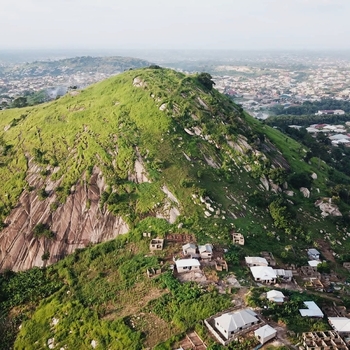 Aerial view of a lush green rocky hill with scattered houses at its base surrounded by a sprawling urban landscape in Ghana. Aerial view of a lush green rocky hill with scattered houses at its base surrounded by a sprawling urban landscape in Ghana.