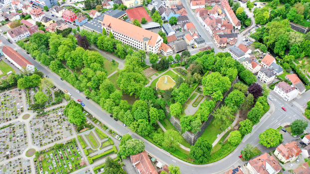 Aerial view of Stadtpark featuring lush green trees a central fountain and historic stone walls surrounded by urban buildings and a cemetery Forchheim Bayern Germany. Aerial view of Stadtpark featuring lush green trees a central fountain and historic stone walls surrounded by urban buildings and a cemetery Forchheim Bayern Germany.