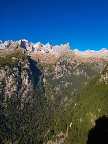Aerial view of the jagged granite peaks and dense evergreen forests of Val di Mello under a clear blue sky in Val Masino Lombardia Italy. Aerial view of the jagged granite peaks and dense evergreen forests of Val di Mello under a clear blue sky in Val Masino Lombardia Italy.